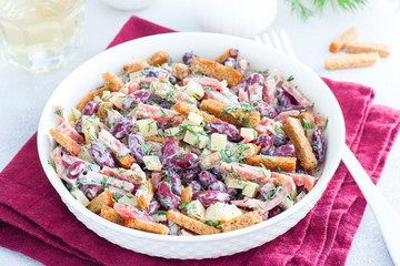 Salad with red beans, smoked sausage, cheese and crackers in a white bowl, horizontal