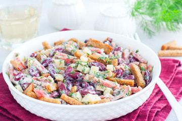 Salad with red beans, smoked sausage, cheese and crackers in a white bowl, horizontal