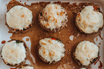 Baked Champignons with cheese and vegetables stuffed on a white plate. Top view