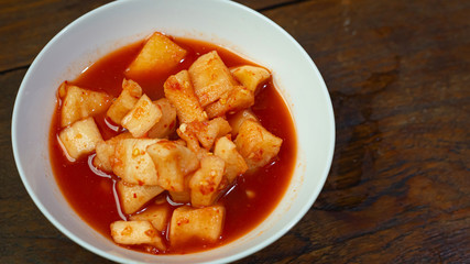 Korean Radish Kimchi in white bowl on wood table for food content.