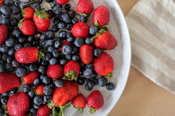 Fresh juicy ripe berries - Blueberries and strawberry оn the white plate on a table background. Top view and copy space. Healthy food concept. Eating lifestyle
