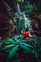 Focus on green leaf on first plan, Silhouette traveller man explore waterfall hidden in tropical rainforest jungle