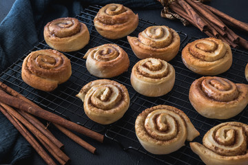 Homemade cinnamon rolls on a colling rack with cinnamon sticks