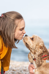 Young woman kissing a dog into nose at the sea shore. The woman petting obedient dog on a sea coast.
