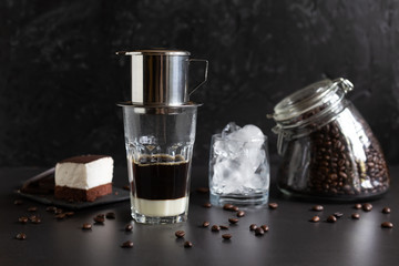 Traditional vietnamese coffee maker placed on the top of glass, glass jar with coffee beans, glass with ice and souffle dessert. Iced coffee for summer. 