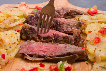 Argentinian Beef slices with potatoes, green pepper, red pepper on a wooden table.