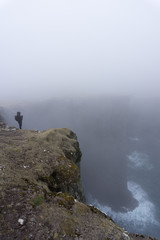 a man standing on the edge of the valley. very hazardous and dangerous. river on the bottom of the valley. Hazardous tourist doesn’t care about safety.