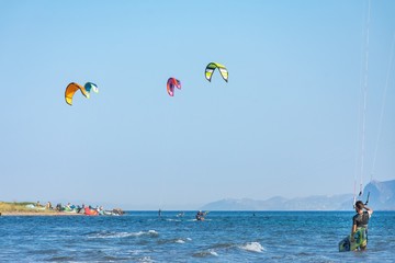 One kitesurfer resting and watching other kitesurfers with colorful kites having fun in Loutsa Greece on a sunny summer day, horizontal