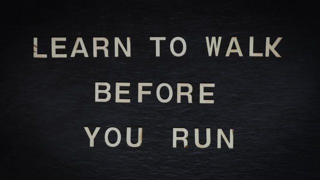 Stop motion of wooden letters writing LEARN TO WALK BEFORE YOU RUN on slate background