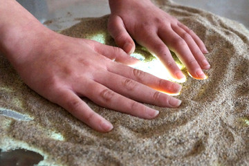  children's hands are engaged in sand therapy on a glass transparent table with backlight