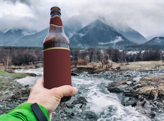 Person holding bottle with beer or other drink at mountains and river background