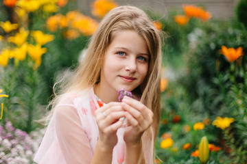 beautiful blue-eyed girl with long blond hair. little girl in a pink flamingo dress. girl in the flower garden. summer bright, emotional photo. large, thick, bright flower garden near the house. 