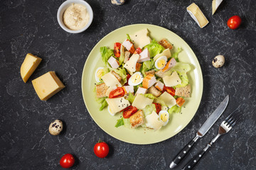 Fresh Caesar salad with delicious chicken breast, ruccola, croutons, egg, parmesan and cherry tomato on black stone background. Top view