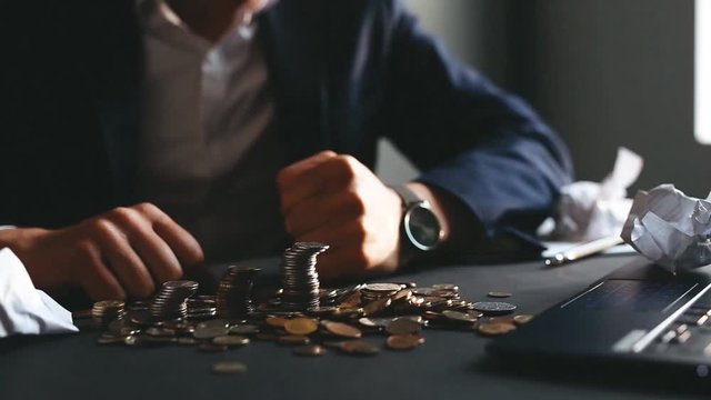 Depressed businessman has lost his business and punches in the stacks with coins. Destroyed businessman. The concept of business loss, bankruptcy and crisis.