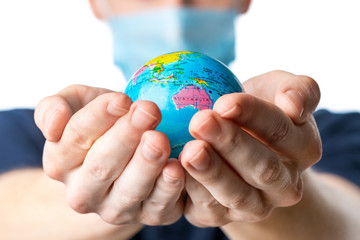 .Close-up of a man's hands holding a small globe, with images Australia, Philippines,a man in a medical mask out of focus, dressed in a blue t-shirt on a white isolated background. 2020. Coronavirus