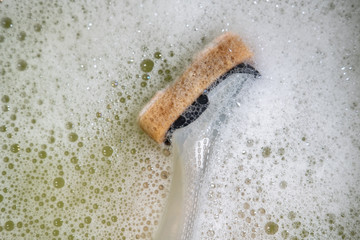 Fototapeta na wymiar Close-up of a generic washing up disk sponge and handle seen in a washing up plastic bowl with plenty of soap suds.