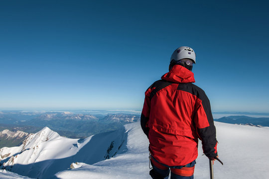 Climber In A Red Jacket Stands On Top Of A Mountain