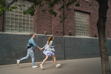 Obraz premium Romantic and happy caucasian couple in casual clothes walking together through the city streets. Love, relationships, romance, happiness concept. Man and woman holding hands and smiling.