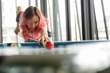 Beautiful woman with pink hair playing billiard