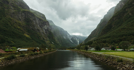 a small river between two mountains in norway at the bottom of the mountains houses
