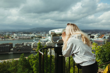 girl looking through binoculars at a city in norway