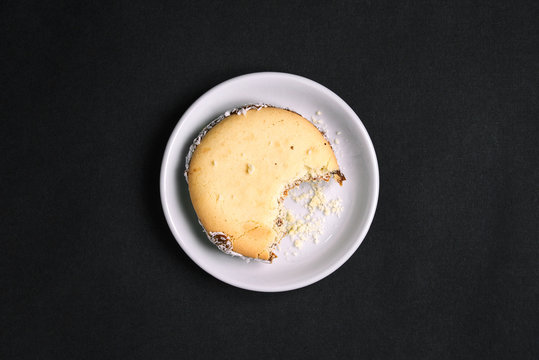 The Bitten-off Cookie Is On A White Plate. Sweet Pastries And Crumbs. Top View On A Black Background. Flat Layout.