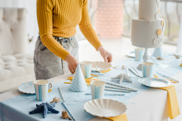 Woman serving party table in blue colors with textile tablecloth, white dishes, glasses for wine...