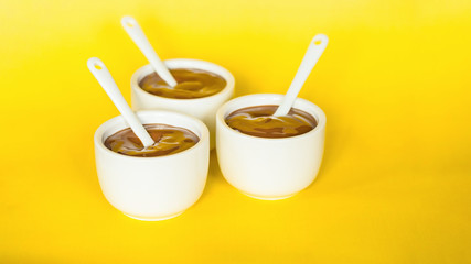 chocolate pudding in white bowls on a yellow background close-up. background with chocolate pudding in bowls and spoons.