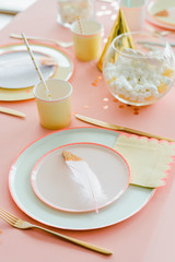 Decorative festive table setting for kids party dinner with textilepink tablecloth, paper colorful plates . Happy birthday for girl or baby shower decoration
