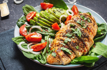 Grilled chicken breast and avocado salad with spinach and cherry tomatoes on black stone background. Healthy food, ketogenic diet