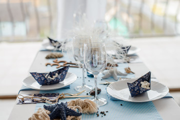 Interior decoration and table setting with white dishes, blue tablecloth and paper decorative boats...