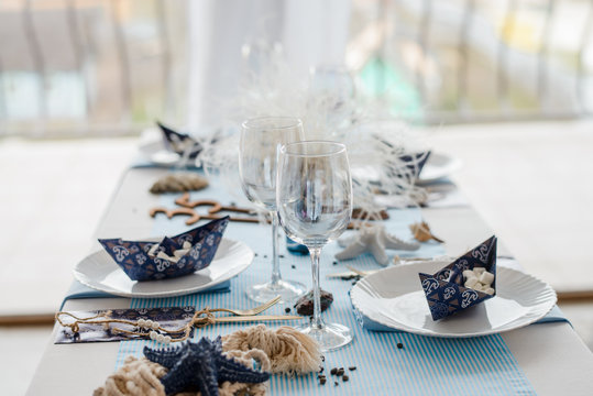 Interior decoration and table setting with white dishes, blue tablecloth and paper decorative boats . Birthday party decoration. Selective focus.