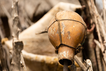Rustic handmade clay pot with twine wrapped to make handle hangs upside down on fence made of sticks outside a small hut in a remote village of Kenya, Africa.