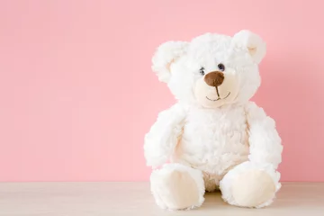 Fotobehang Smiling white teddy bear sitting on table at pastel pink wall background. Kids best friend. Front view. Close up. © fotoduets