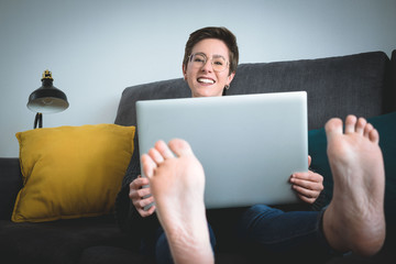 Feet of a woman teleworking with the laptop on the sofa at home
