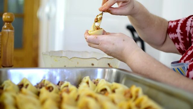 Preparation of homemade lumaconi filled in with tomato sauce and minced meat. Close up of man's hands stuffing homemade Italian pasta recipe