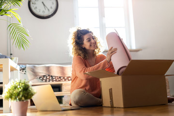 Woman unpacking box with workout equipment at home 
