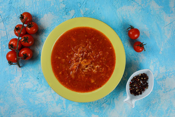 Delicious, tasty tomato soup on the green plate on the blue background. Tomatoes and decorative plate with pepper next to the meal.