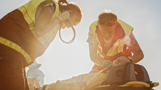 On the Car Crash Traffic Accident Scene: Paramedics Saving Life of a Traffic Accident Victim who is Lying on Stretchers. They Listen To a Heartbeat, Apply Oxygen Mask and Give First Aid Help