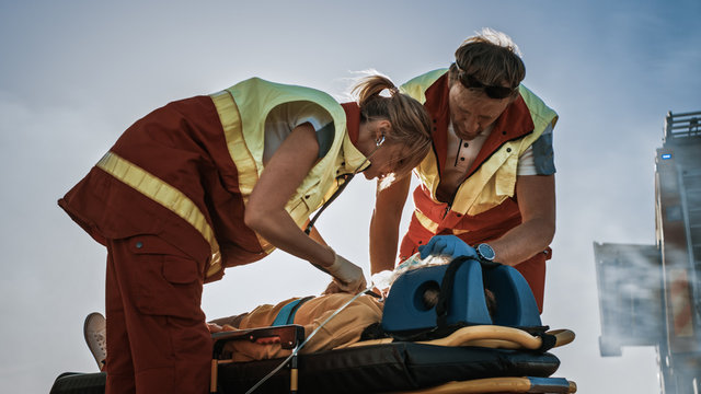 On the Car Crash Traffic Accident Scene: Paramedics Saving Life of a Traffic Accident Victim who is Lying on Stretchers. They Listen To a Heartbeat, Apply Oxygen Mask and Give First Aid Help