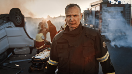 Portrait of the Brave Firefighter Walking to the Camera. In Background Courageous Heroes Paramedics and Firemen Rescue Team Fight Fire, Smoke and Save People’s Lives