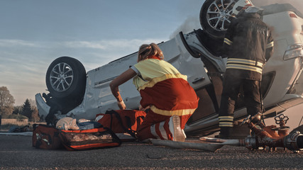 Car Crash Traffic Accident: Paramedics and Firefighters Rescue Passengers Trapped in Burning Rollover Vehicle. Medics Prepare First Aid Tools. Low Angle Shot