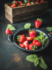 Wooden box with fresh strawberries and black bowl of strawberries on vintage table.