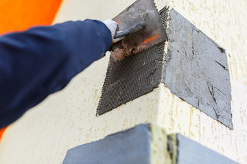 Male builder smear gray wet plaster with a spatula on the facade of the house