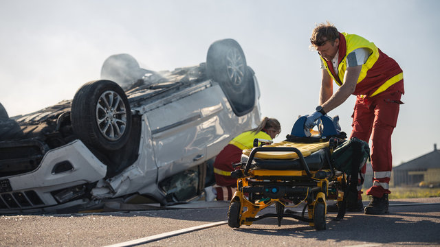 Paramedics and Firefighters Arrive On the Car Crash Traffic Accident Scene. Professionals Prepairing Stretchers For Rescue Injured Victim Trapped in Rollover Vehicle.