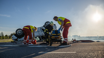 On the Car Crash Traffic Accident Scene: Team of Paramedics and Firefighters Rescue Injured People Trapped in Rollover Vehicle. Professionals Extricate Victims, Give First Aid. © Gorodenkoff