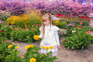 Happy little girl in flowers in a summer garden