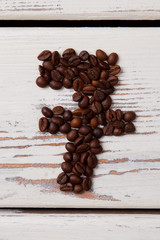 Number seven made of roasted coffee beans. White wooden planks. Vertical image.