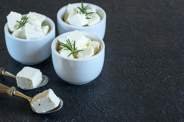 white bowls with feta cheese slices and rosemary sprigs, spoons with feta slices close-up. feta cheese in bowls and spoons on the table close-up.