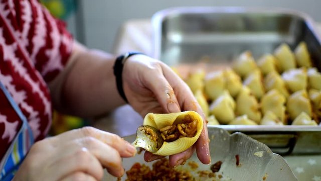 Preparation of homemade lumaconi filled in with tomato sauce and minced meat. Close up of man's hands stuffing homemade Italian pasta recipe